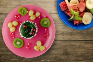 Kek ve meyve üzümleri, kivi, ahşap zemin üzerinde nar. Meyveli tatlı pembe tabak manzaralı.