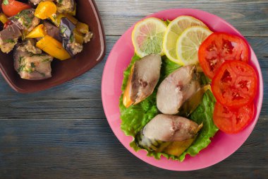 Sebze salatası manzaralı pembe tabakta tütsülenmiş uskumru. Mavi ahşap arka planda limonlu uskumru ve domates.