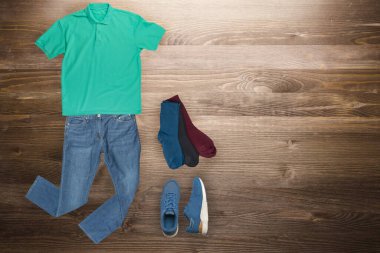 Düz yatış, erkek modası. Mavi kot pantolon, mavi spor ayakkabı, yeşil tişört, ahşap arka planda birkaç renk çorap. Günlük kıyafet üst görünüm