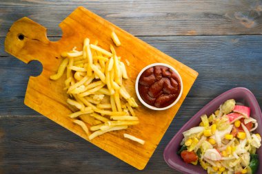 Gri mavi ahşap arka planda ketçaplı patates kızartması. Kahverengi ahşap tabakta patates kızartması ve vejetaryen salata.