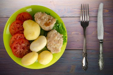 Kireç tabağında patates ve çatal ve bıçak manzaralı pirzola. Patatesli pirzola ve mor ahşap arka plan.