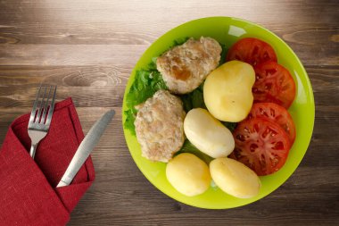 Kireç tabağında patates ve çatal ve bıçak manzaralı pirzola. Kahverengi ahşap arka planda patatesli pirzola