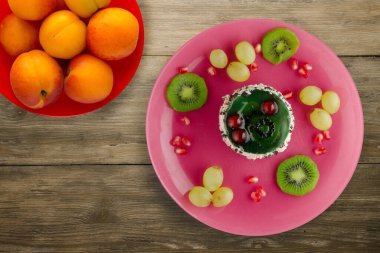 Kek ve meyve üzümleri, kivi, ahşap zemin üzerinde nar. Meyveli tatlı pembe tabak manzaralı.