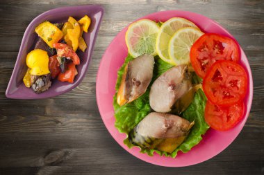 Pembe tabakta tütsülenmiş uskumru. Sebze salatanın üst manzarası. Siyah ahşap arka planda limonlu uskumru ve domates.