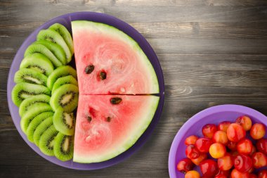 Karpuz ve kivi siyah ahşap bir zemin üzerinde mor bir tabakta dilimlendi.