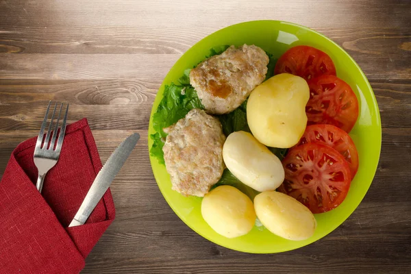 Kireç tabağında patates ve çatal ve bıçak manzaralı pirzola. Kahverengi ahşap arka planda patatesli pirzola