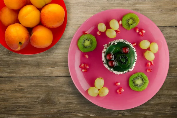 Kek ve meyve üzümleri, kivi, ahşap zemin üzerinde nar. Meyveli tatlı pembe tabak manzaralı.