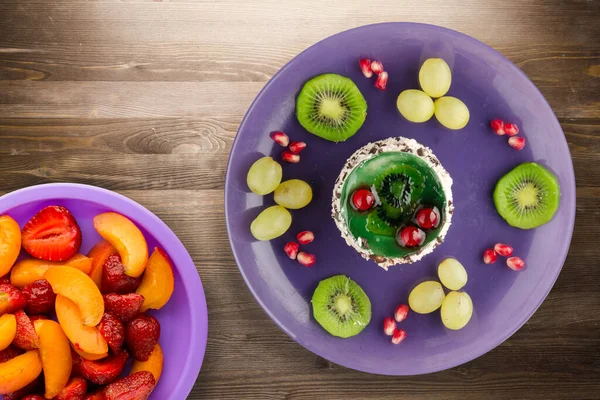 Kek ve meyve üzümleri, kivi, kahverengi ahşap zemin üzerinde nar. Mor tabak manzaralı meyveli tatlı.