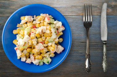 Çatal ve bıçak manzaralı lacivert tabakta yengeç salatası. Gri ve mavi ahşap arka planda yengeç salatası