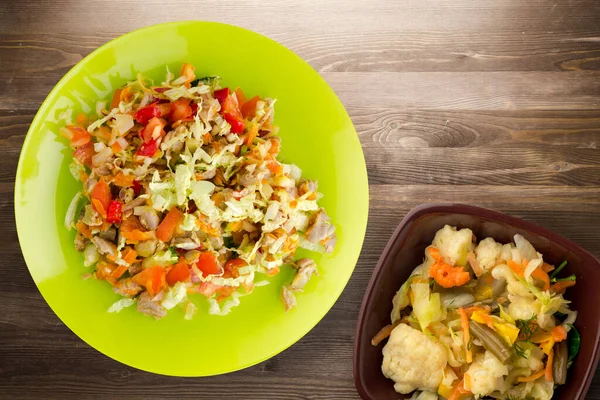 salad with chicken stomachs with vegetables carrots, onions, peppers, cabbage, tomato, broccoli. salad with chicken on lime plate on brown wooden background. healthy salads top view