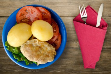  Çatal ve bıçak manzaralı mavi tabakta patatesli pirzola. Tahta arka planda patatesli pirzola.