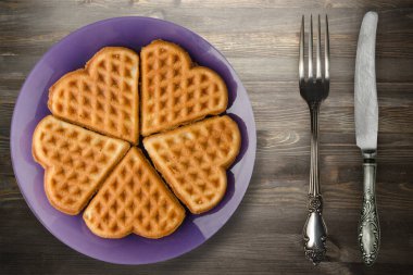 Siyah ahşap arka planda çatal ve bıçaklı Belçika waffleları. Mor bir tabakta waffle.