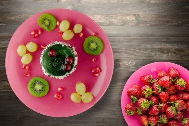 Kek ve meyve üzümleri, kivi, siyah ahşap zemin üzerinde nar. Pembe tabakta meyveli tatlı.