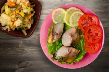 Pembe tabakta tütsülenmiş uskumru. Sebze salatanın üst manzarası. Siyah ahşap arka planda limonlu uskumru ve domates.