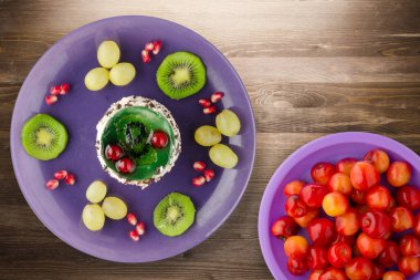 Kek ve meyve üzümleri, kivi, kahverengi ahşap zemin üzerinde nar. Mor tabak manzaralı meyveli tatlı.