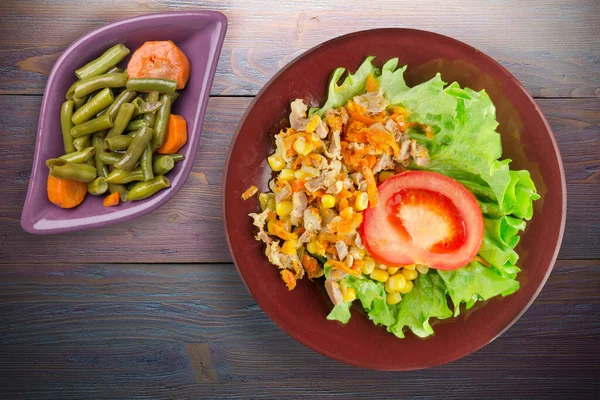 salad with chicken stomachs with carrots and corn and salad on brown plate with vegetable salad top view. chicken salad with vegetables on purple wooden background