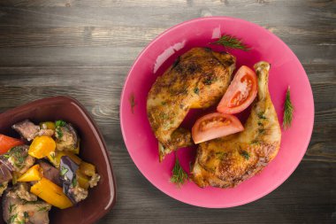 Siyah ahşap arka planda sebzeli tavuk budu. Tavuk budu pembe tabakta, sebze salatası manzaralı.