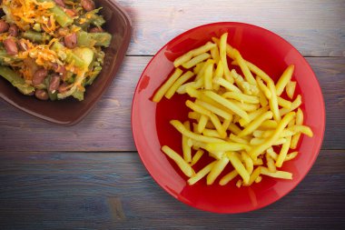  Ahşap arka planda patates kızartması. Kırmızı tabakta patates kızartması ve vejetaryen salatası.