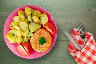 Yeşil ahşap arka planda patates köftesi. Çatal ve bıçak manzaralı pembe tabakta bir dilim domatesli köfte.