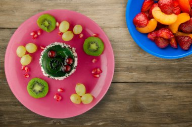 Kek ve meyve üzümleri, kivi, ahşap zemin üzerinde nar. Meyveli tatlı pembe tabak manzaralı.