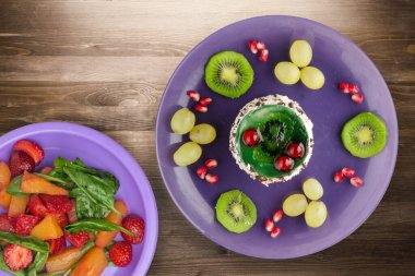 Kek ve meyve üzümleri, kivi, kahverengi ahşap zemin üzerinde nar. Mor tabak manzaralı meyveli tatlı.