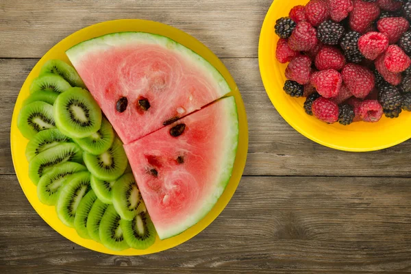 Karpuz ve kivi kahverengi ahşap bir arka planda sarı bir tabakta dilimlenmiş. Karpuz ve meyvelerle dilimlenmiş kivi.