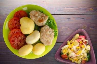  Limonlu patatesli pirzola ve sebze salatası. Patatesli pirzola ve mor ahşap arka plan.