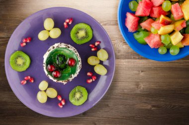 Kek ve meyve üzümleri, kivi, kahverengi ahşap zemin üzerinde nar. Mor tabak manzaralı meyveli tatlı.