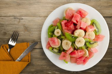 Kahverengi ahşap zemin üzerinde sağlıklı taze meyve salatası. Çatallı ve diz kapaklı meyve salatası.