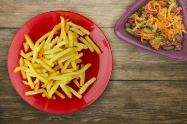  Ahşap arka planda patates kızartması. Sebze salatası manzaralı kırmızı tabakta patates kızartması.