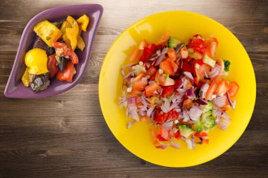 Vejetaryen yemeği. Biberli salata, domates, soğan, sarı tabakta sebze salatası manzaralı brokoli. Kahverengi ahşap arka planda vegan salatası