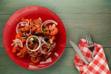 Çatal ve bıçak manzaralı vejetaryen yemekleri. Domates, soğan, yeşil ahşap arka planda kırmızı tabakta rezene. sağlıklı yiyecekler