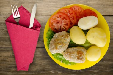  Çatal ve bıçak manzaralı sarı tabakta patatesli pirzola. Kahverengi ahşap arka planda patatesli pirzola