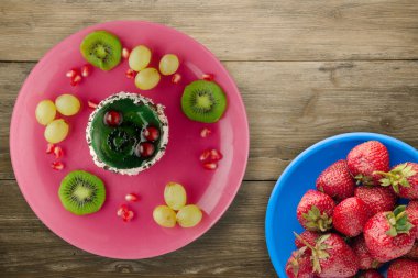 Kek ve meyve üzümleri, kivi, ahşap zemin üzerinde nar. Meyveli tatlı pembe tabak manzaralı.