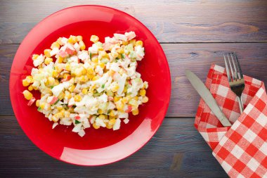 Çatal ve bıçak manzaralı kırmızı tabakta yengeç salatası. Mor ahşap arka planda yengeç salatası