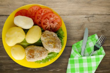 Çatal ve bıçak manzaralı sarı tabakta patatesli pirzola. Kahverengi ahşap arka planda patatesli pirzola