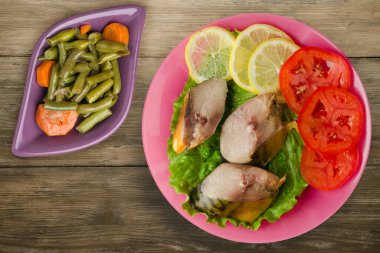 Sebze salatası manzaralı pembe tabakta tütsülenmiş uskumru. Kahverengi ahşap arka planda limonlu uskumru ve domates.