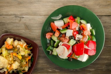 Kahverengi ahşap arka planda Yunan salatası. Vejetaryen salata manzaralı yeşil tabakta Yunan salatası. sağlıklı yiyecekler