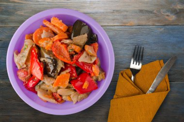 Mavi gri ahşap arka planda sebze güveci. Mor tabakta çatal ve bıçak manzaralı Bulgarca güveç