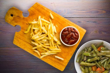 Patates kızartması ve mor ahşap arka planda ketçap. Kahverengi ahşap tabakta patates kızartması ve vejetaryen salata.