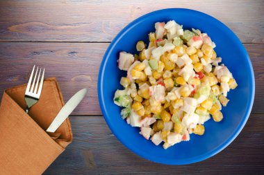 Çatal ve bıçak manzaralı lacivert tabakta yengeç salatası. Mor ahşap arka planda yengeç salatası