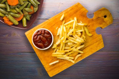 Patates kızartması ve mor ahşap arka planda ketçap. Kahverengi ahşap tabakta patates kızartması ve vejetaryen salata.
