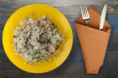 salata daikon, soğan ve dereotu mavi gri ahşap arka planda. Çatal ve bıçak manzaralı sarı tabakta salata.