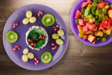 Kek ve meyve üzümleri, kivi, kahverengi ahşap zemin üzerinde nar. Mor tabak manzaralı meyveli tatlı.