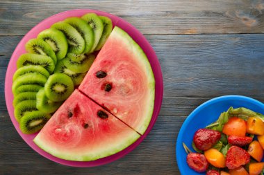 Kırmızı bir tabakta karpuz ve kivi dilimlenmiş mavi gri ahşap arka plan manzaralı meyve salatası.