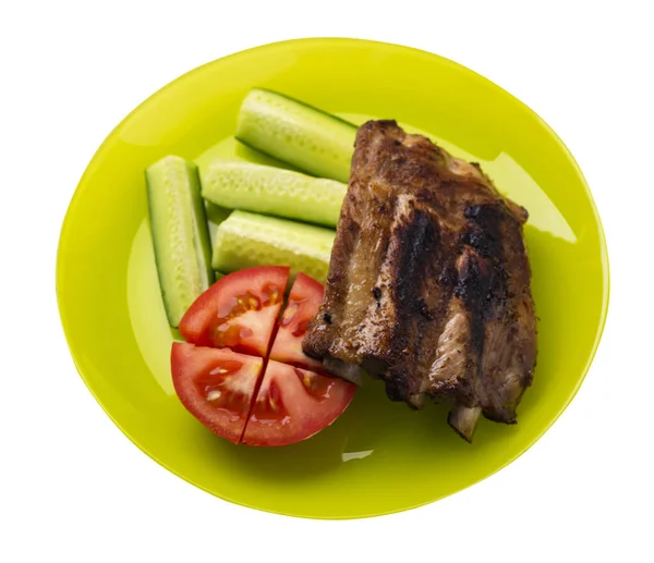 grilled pork ribs with sliced cucumbers and tomatoes on yellow plate. pork ribs isolated on white background. ribs grill top side view