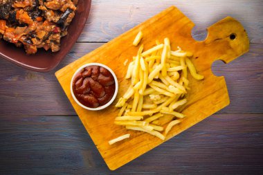 Patates kızartması ve mor ahşap arka planda ketçap. Kahverengi ahşap tabakta patates kızartması ve vejetaryen salata.