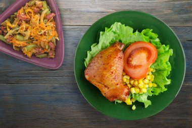 Salatalı tavuk kanadı, yeşil tabakta mısır ve domates ve sebze salatası. Gri mavi ahşap arka planda sebzeli tavuk kanadı
