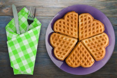 Belçika waffle 'ı mavi ahşap arka plan. Çatal ve bıçak manzaralı mor bir tabakta waffle.