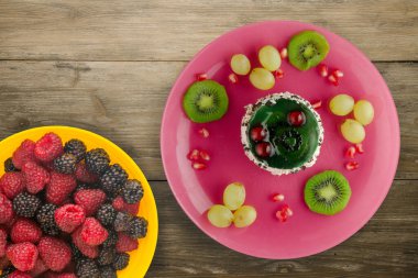 Kek ve meyve üzümleri, kivi, ahşap zemin üzerinde nar. Meyveli tatlı pembe tabak manzaralı.